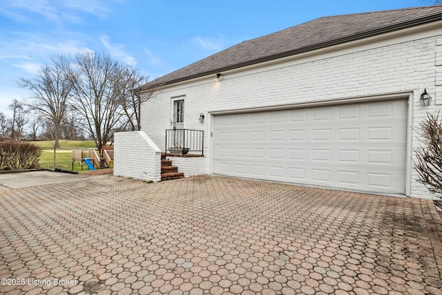 view of property exterior featuring a garage, decorative driveway, brick siding, and a playground