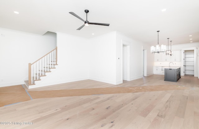 unfurnished living room with sink, crown molding, light hardwood / wood-style floors, and ceiling fan with notable chandelier