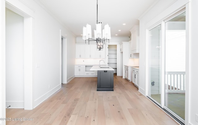 kitchen featuring hanging light fixtures, white cabinetry, crown molding, and a kitchen island with sink