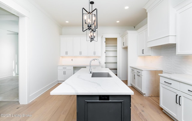 kitchen featuring an island with sink, hanging light fixtures, light stone countertops, sink, and white cabinets