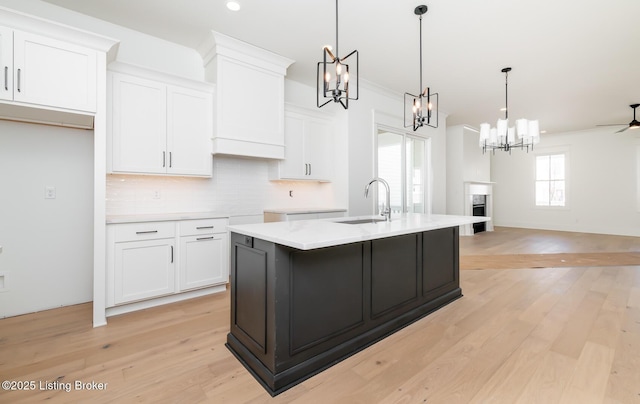 kitchen with decorative light fixtures, sink, an island with sink, and white cabinets