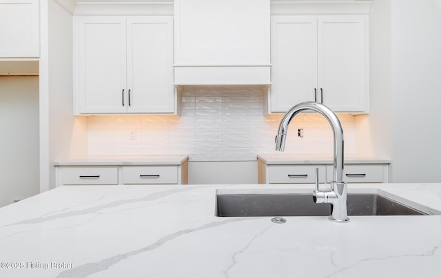 kitchen featuring decorative backsplash, sink, light stone countertops, and white cabinets