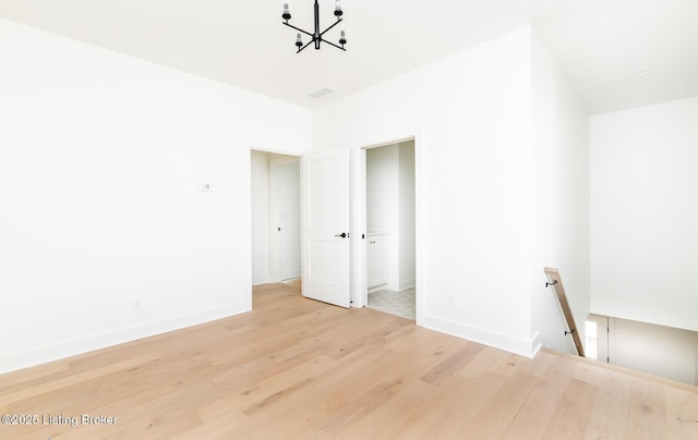 spare room with an inviting chandelier and light hardwood / wood-style flooring