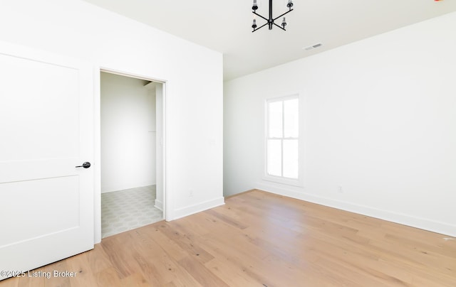 empty room featuring an inviting chandelier and light hardwood / wood-style flooring