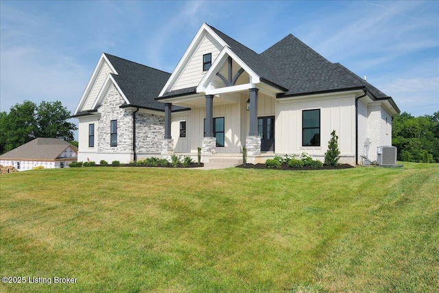 view of front of house with stone siding, roof with shingles, cooling unit, board and batten siding, and a front yard