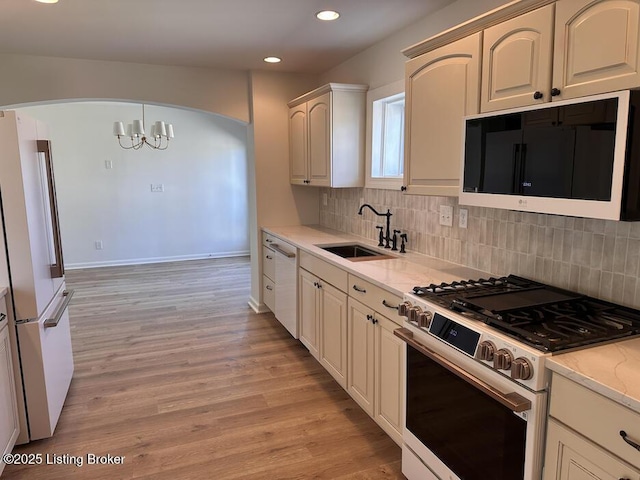 kitchen with white appliances, tasteful backsplash, light wood finished floors, hanging light fixtures, and a sink