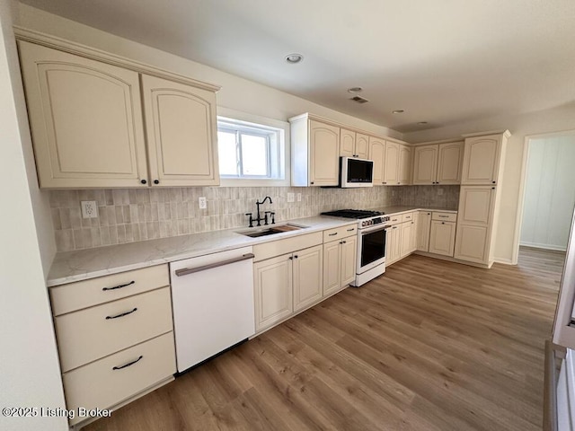 kitchen with decorative backsplash, cream cabinets, dark wood-type flooring, a sink, and white appliances