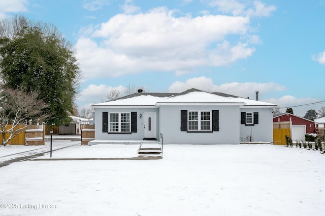 snow covered house with fence and stucco siding