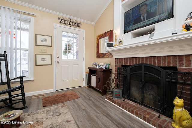 entryway featuring a brick fireplace, crown molding, wood-type flooring, and a healthy amount of sunlight