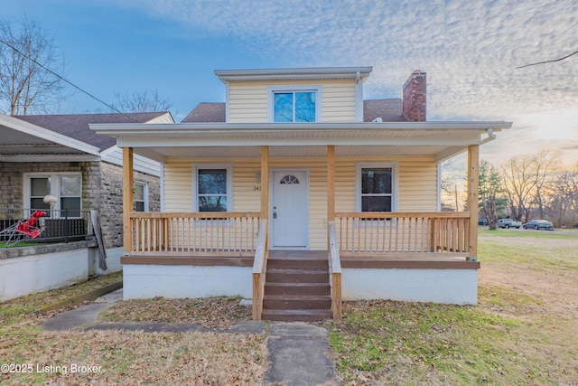 bungalow-style home with covered porch, a shingled roof, and a chimney