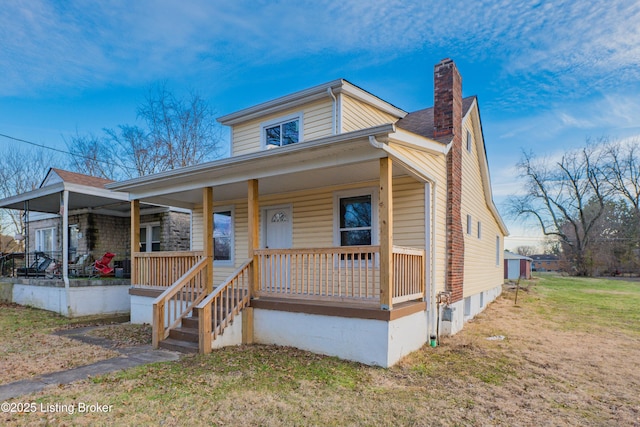 view of front of property with a porch, a chimney, and a front lawn