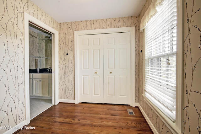 interior space with dark wood-type flooring, visible vents, baseboards, and wallpapered walls