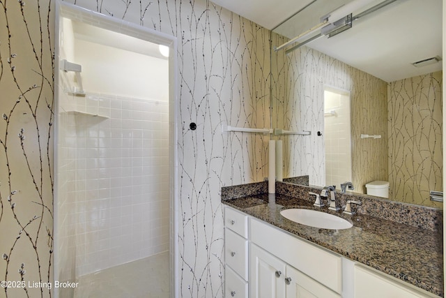 full bathroom featuring visible vents, toilet, vanity, a walk in shower, and wallpapered walls