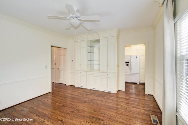 spare room with baseboards, visible vents, a ceiling fan, ornamental molding, and dark wood-style flooring