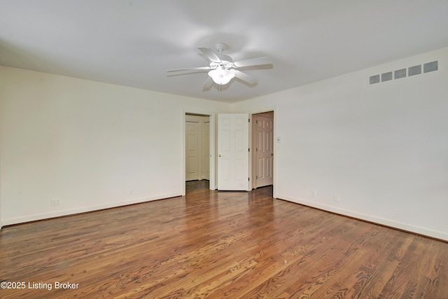 spare room with dark wood-style floors, ceiling fan, visible vents, and baseboards