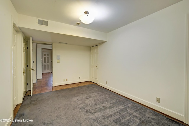 spare room featuring dark carpet, visible vents, and baseboards