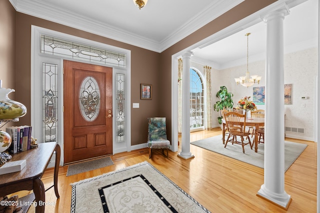 foyer entrance featuring decorative columns, visible vents, light wood-style flooring, an inviting chandelier, and ornamental molding