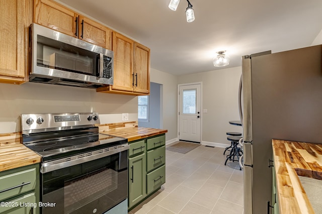 kitchen with wood counters, light tile patterned floors, stainless steel appliances, and green cabinets