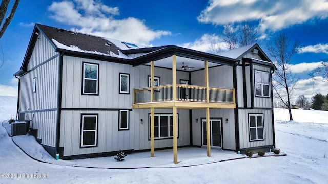 snow covered rear of property featuring a balcony, cooling unit, and board and batten siding