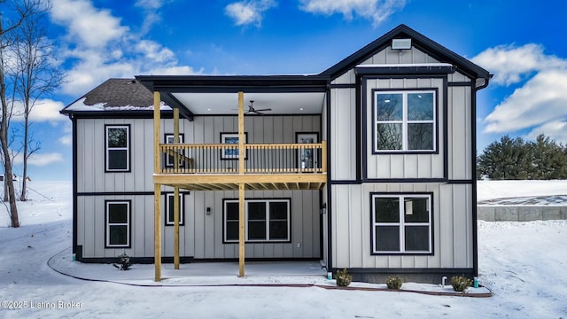 snow covered back of property featuring board and batten siding, roof with shingles, and a balcony