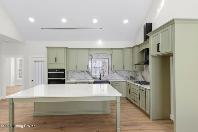 kitchen with wall chimney range hood, green cabinets, and a sink