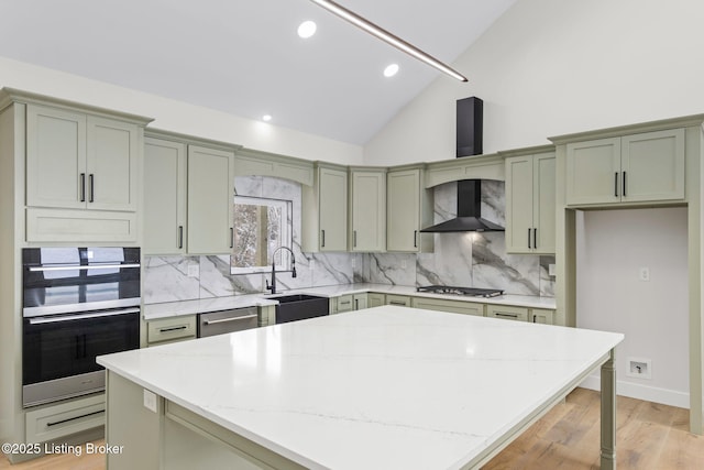 kitchen featuring a center island, a sink, wall chimney range hood, and light stone countertops