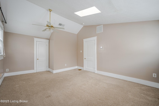 empty room featuring ceiling fan, lofted ceiling with skylight, and light colored carpet