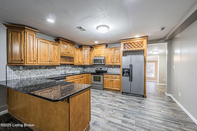 kitchen with kitchen peninsula, stainless steel appliances, light hardwood / wood-style floors, sink, and dark stone counters