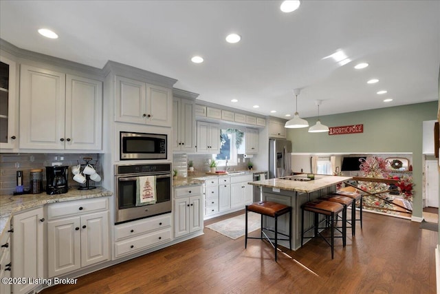 kitchen featuring a kitchen island, stainless steel appliances, a breakfast bar area, dark hardwood / wood-style flooring, and hanging light fixtures