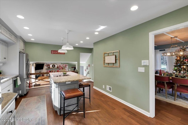 kitchen with decorative light fixtures, a kitchen island, a kitchen breakfast bar, light stone counters, and gray cabinets