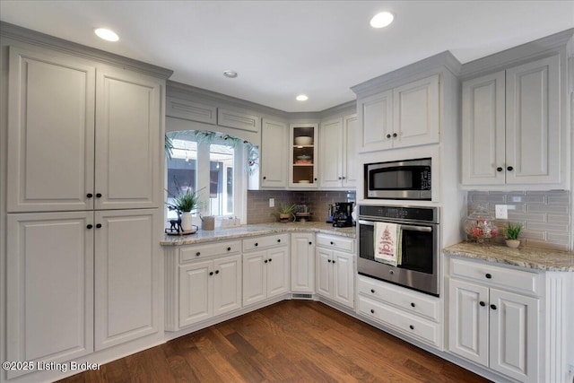 kitchen featuring appliances with stainless steel finishes, tasteful backsplash, dark wood-type flooring, white cabinets, and light stone countertops