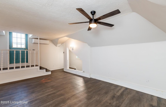 additional living space with a wall unit AC, vaulted ceiling, ceiling fan, a textured ceiling, and dark hardwood / wood-style floors