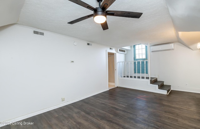 empty room featuring a wall mounted AC, vaulted ceiling, ceiling fan, a textured ceiling, and dark hardwood / wood-style floors