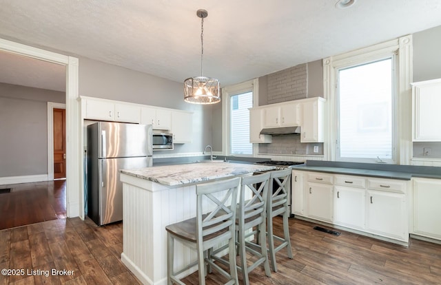 kitchen featuring appliances with stainless steel finishes, white cabinetry, pendant lighting, dark hardwood / wood-style flooring, and decorative backsplash