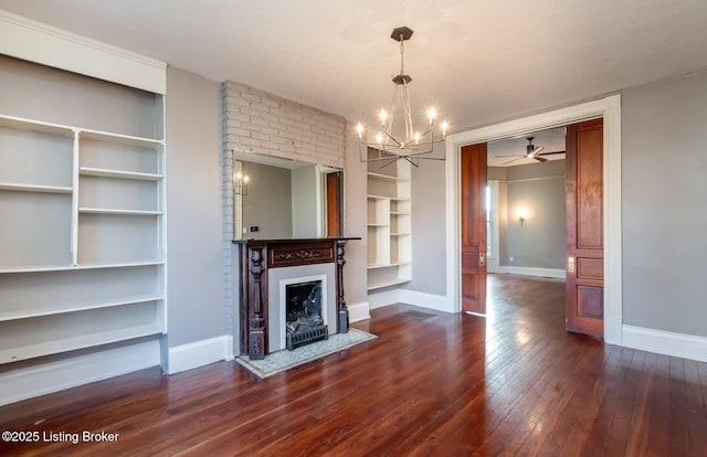 unfurnished living room with ceiling fan with notable chandelier, dark wood-type flooring, and built in shelves