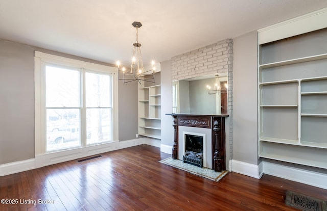 unfurnished living room featuring dark wood-type flooring, built in features, and a notable chandelier