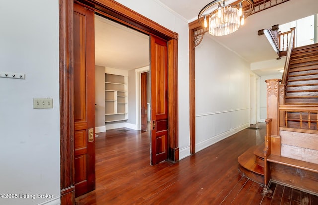 hallway with built in features, ornamental molding, an inviting chandelier, and dark hardwood / wood-style flooring