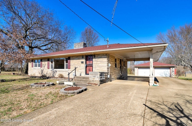 ranch-style house with concrete driveway, stone siding, a chimney, an attached carport, and an outbuilding