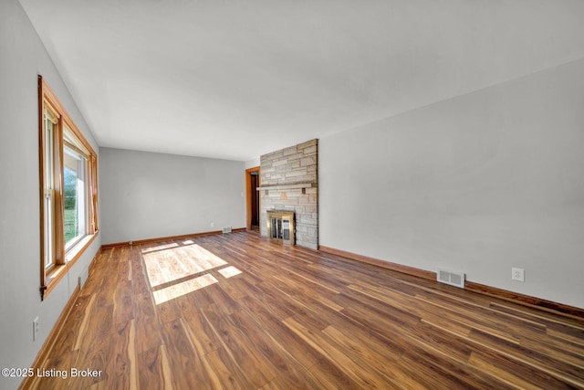 unfurnished living room with baseboards, visible vents, dark wood-type flooring, and a stone fireplace