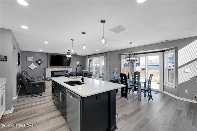 kitchen featuring a kitchen island with sink, decorative light fixtures, a stone fireplace, sink, and dishwasher