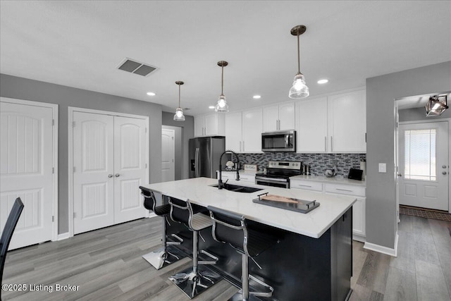 kitchen featuring hanging light fixtures, stainless steel appliances, white cabinets, and a kitchen island with sink