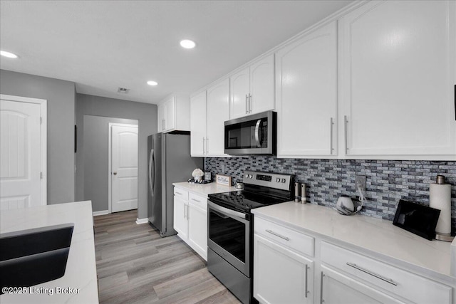 kitchen with light hardwood / wood-style flooring, stainless steel appliances, white cabinetry, and backsplash