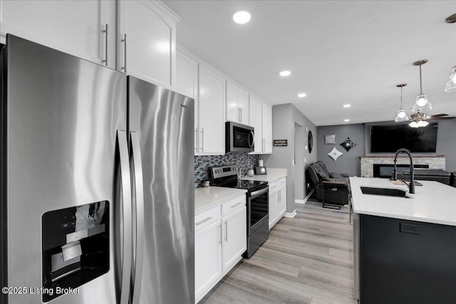 kitchen featuring appliances with stainless steel finishes, sink, backsplash, white cabinetry, and pendant lighting