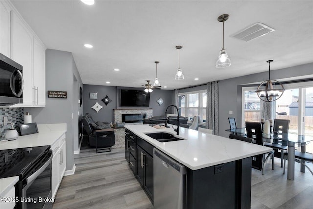 kitchen featuring a center island with sink, hanging light fixtures, sink, appliances with stainless steel finishes, and white cabinets