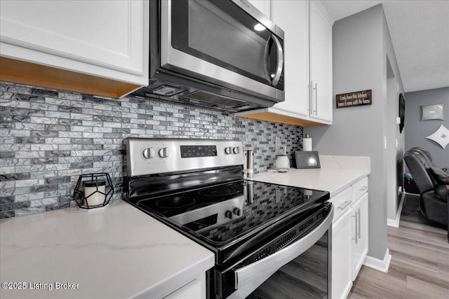 kitchen with light hardwood / wood-style flooring, light stone counters, white cabinetry, stainless steel appliances, and decorative backsplash