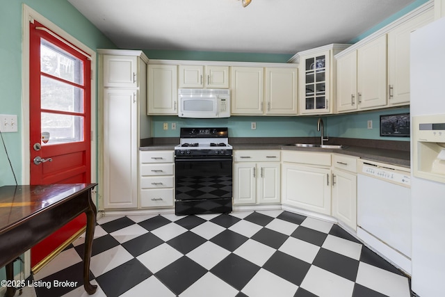 kitchen featuring dark countertops, white appliances, dark floors, and a sink