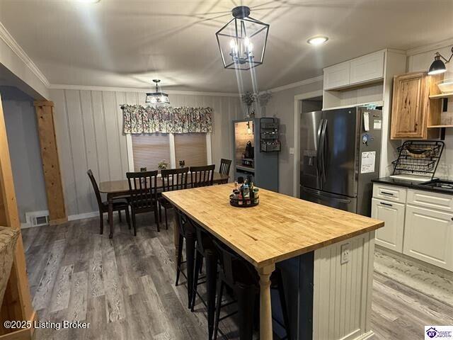 kitchen featuring butcher block countertops, a kitchen island, stainless steel fridge, a kitchen bar, and pendant lighting