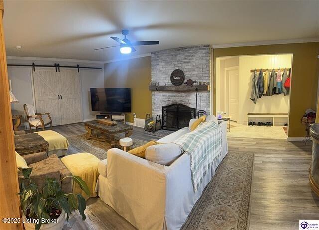 living room featuring ornamental molding, ceiling fan, hardwood / wood-style floors, a barn door, and a brick fireplace