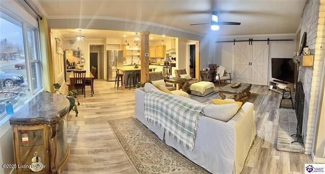 living room featuring ceiling fan, a barn door, ornamental molding, and light hardwood / wood-style flooring