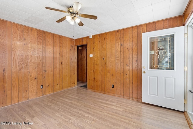 unfurnished room featuring light wood-style floors, a ceiling fan, and wooden walls